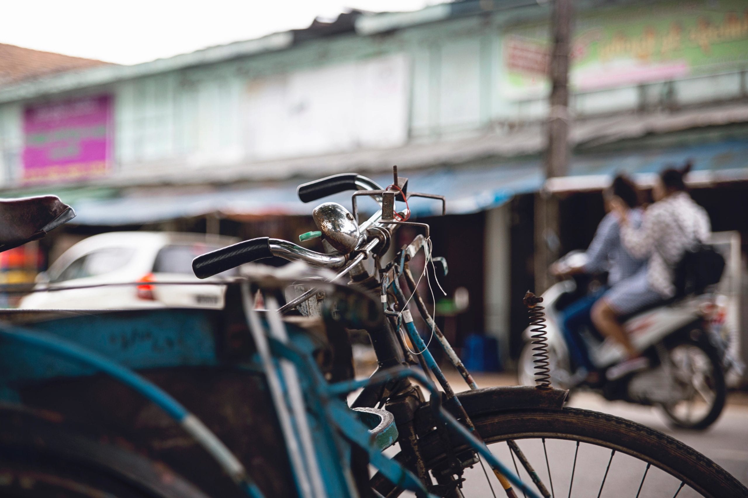 Digital identity in the last mile: lessons from South East Asia a decorative image of a street, somewhere in south-east Asia. In the foreground is a cycle and in the background is a parade of shops.