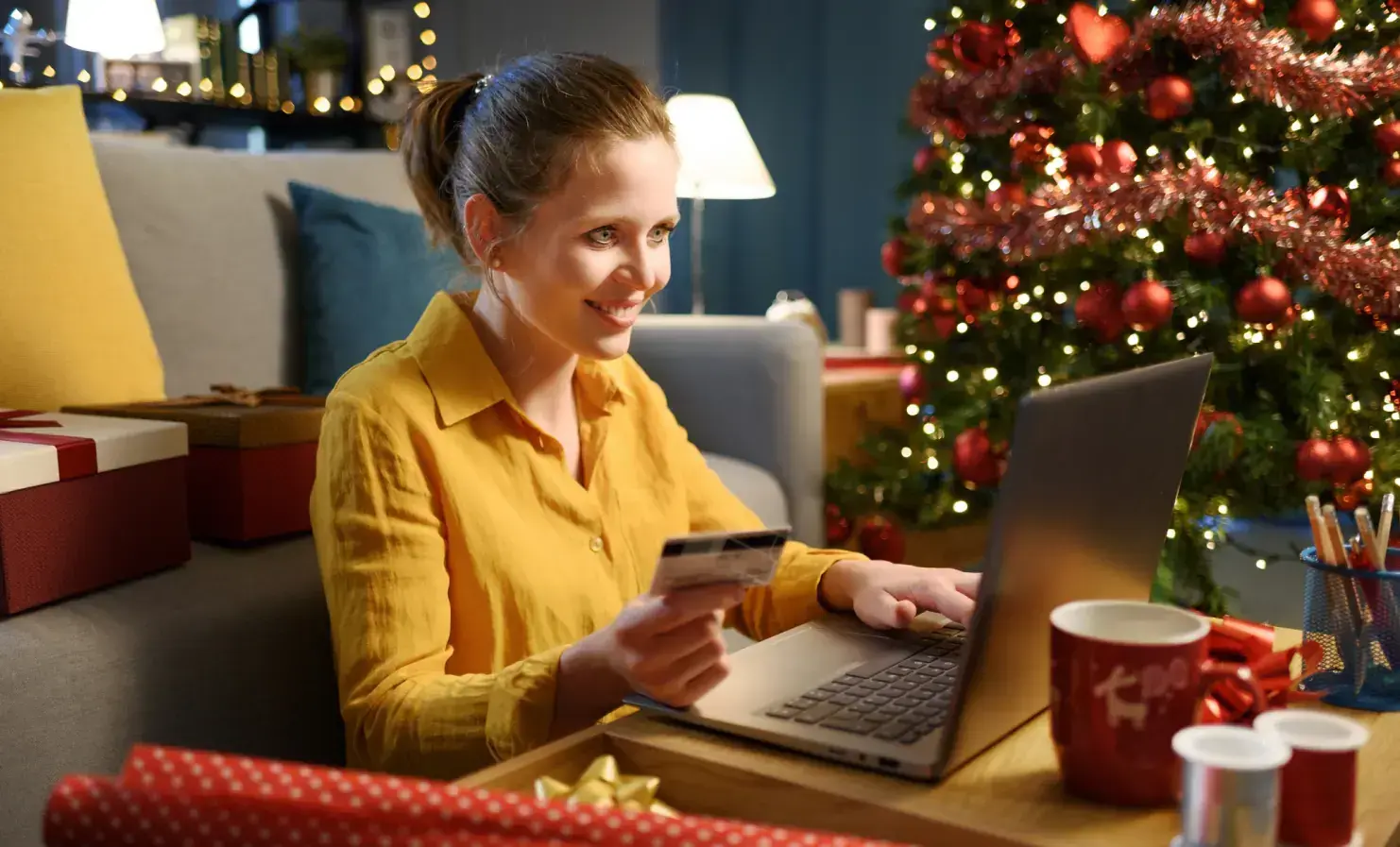 Woman sat on her laptop next to a christmas tree using her credit card to purchase something online