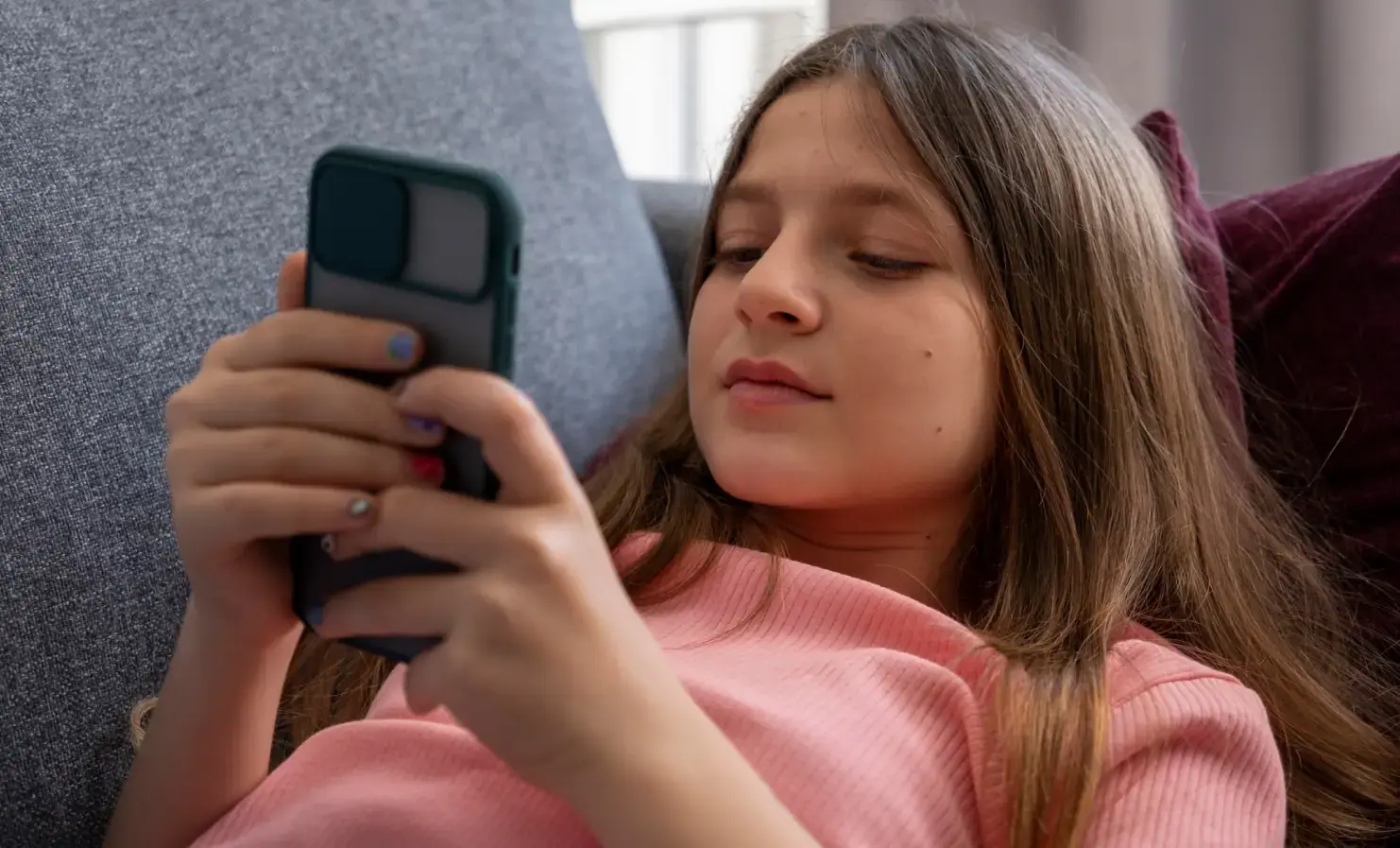 An image of a young girl lying on a sofa and using a smartphone.