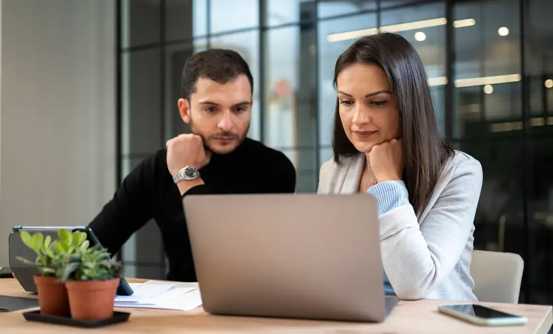 An image of two people in an office, sitting at a desk and working together with a laptop.