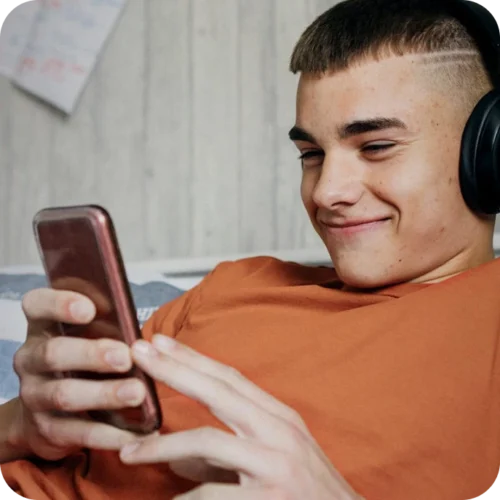 Teenage boy lounging whilst looking at his phone and wearing over-ear headphones