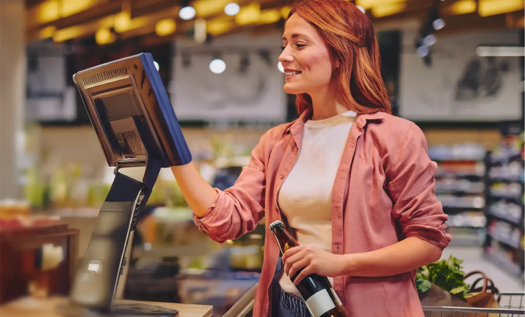 An image of a woman trying to buy a bottle of alcohol at a supermarket self-checkout terminal.