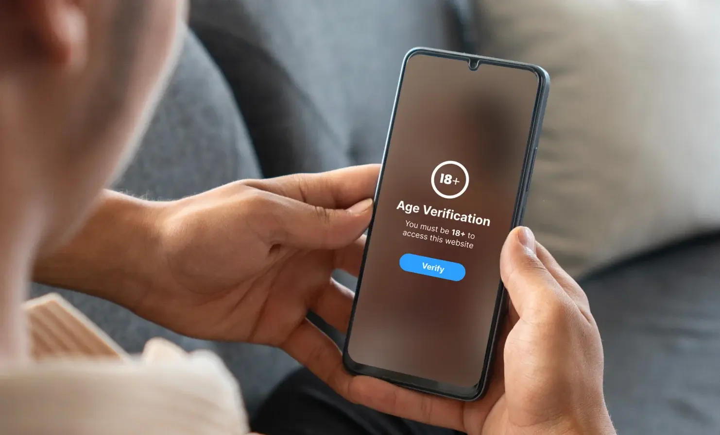 An image of someone holding their mobile phone. On the screen, the platform is asking for the user to verify their age to access age-restricted content.