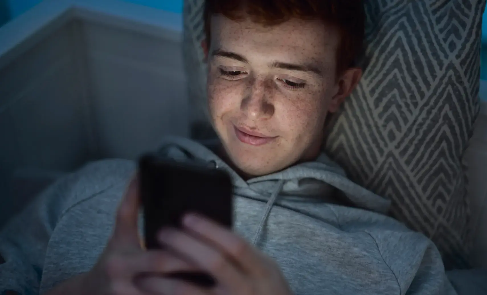 An image of a teenager holding and using his mobile phone.
