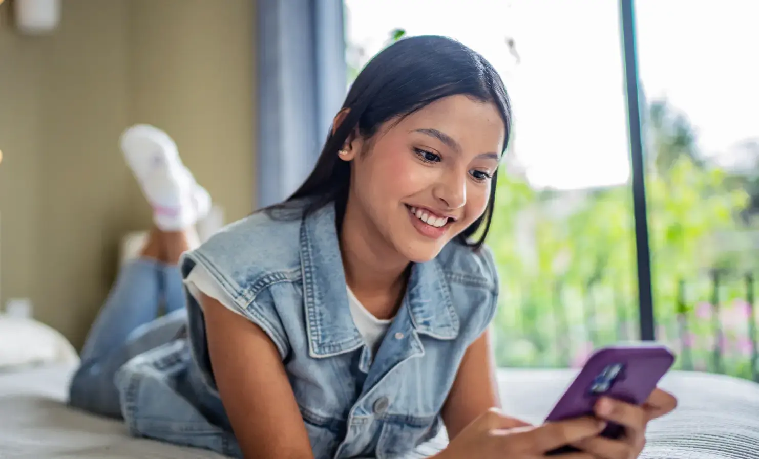 An image of a girl lying on a bed and using a mobile phone.