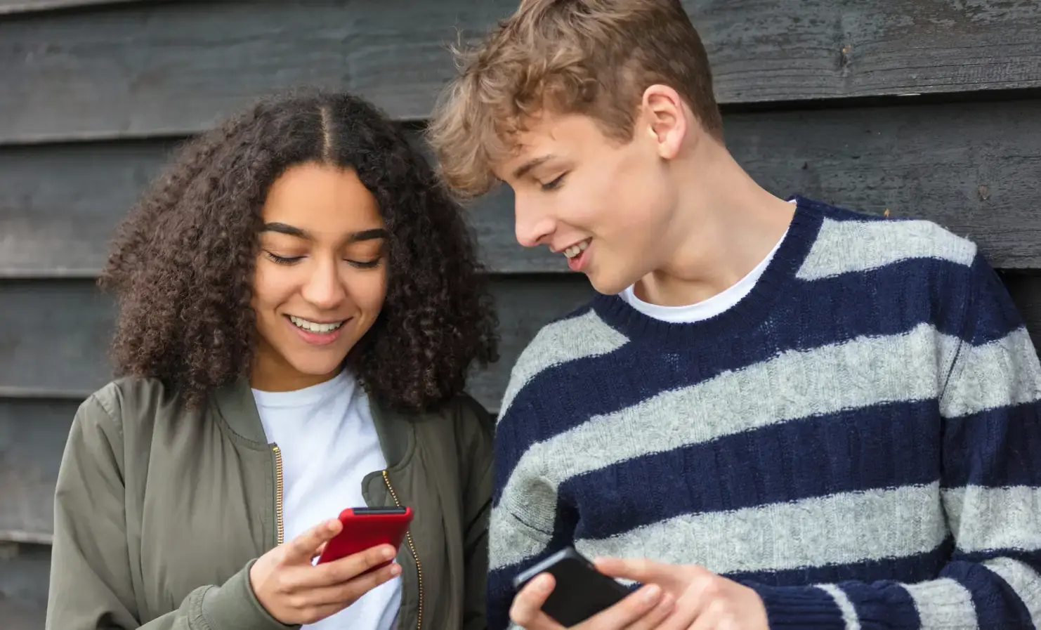 An image of two young people holding their mobile phones and smiling
